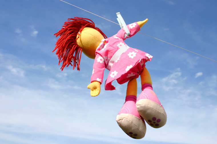 Colorful doll hanging on the laundry wire against blue sky and drying